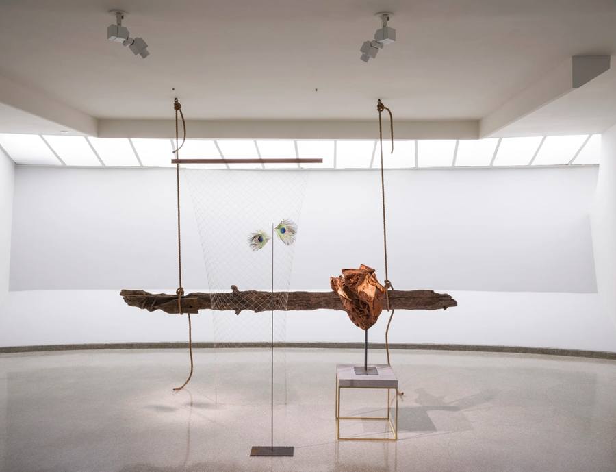Carol Bove, an early assemblage of a driftwood log suspended by ropes with netting, two peacock feathers and a crumpled copper form, in the Guggenheim rotunda