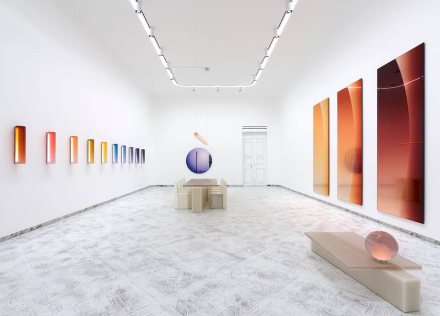 Installation view of Sabine Marcelis, Phases, at Salon 94 Design: a white gallery with a row of small gradient resin wall panels, a violet resin disc suspended above a pale table, three tall amber and red tinted mirrors, and a pink resin sphere resting on a low bench