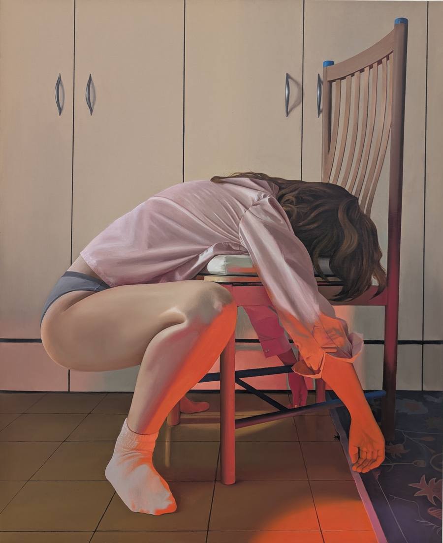 Photorealistic oil painting by Noa Wiegenfeld of a young woman in a pink satin shirt curled forward over a wooden chair in a bedroom, her face hidden by her hair, an intense orange light falling across her legs and the floor