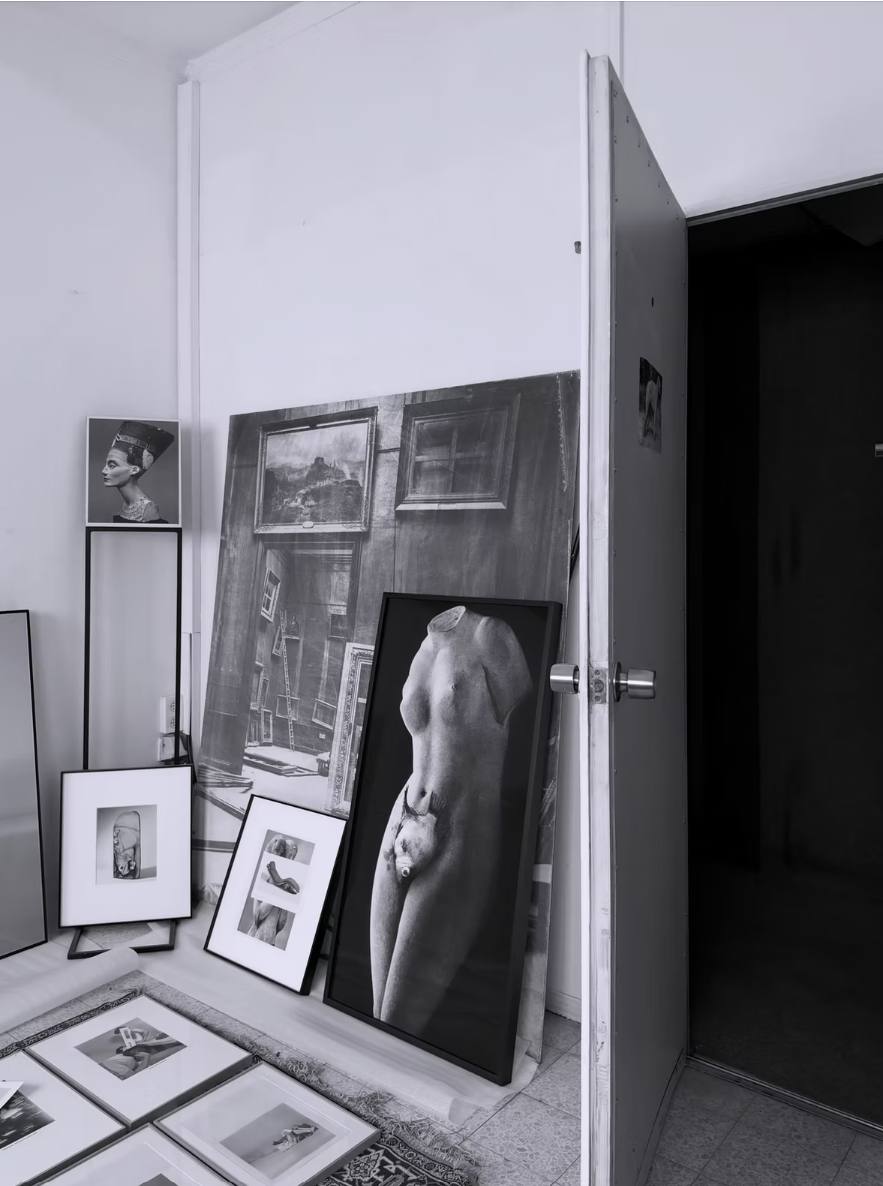 Installation view from Dana Darvish's studio: framed black and white photographs, including a Nefertiti bust and a nude torso, leaning against white walls beside an open door