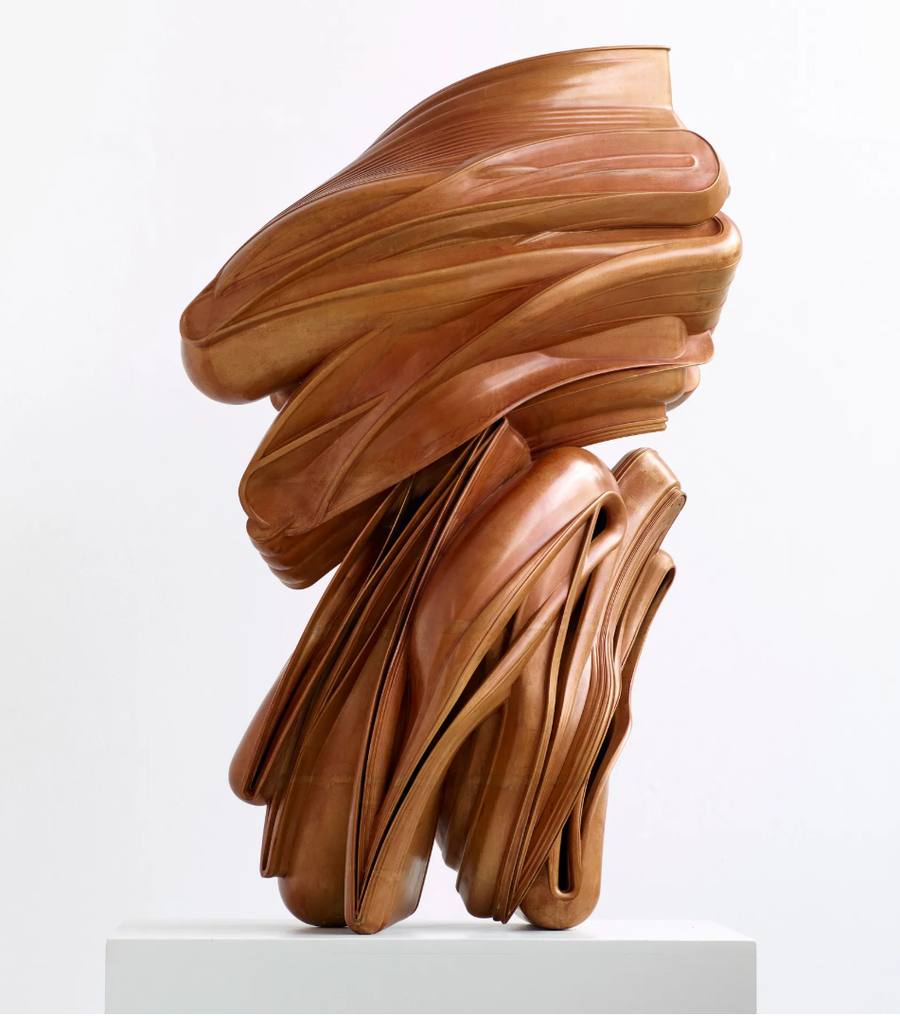 Tony Cragg bronze sculpture, a tall twisting stack of smooth ribbon-like layers in warm reddish brown that seem to flow and fold like fabric or wood grain, on a white plinth