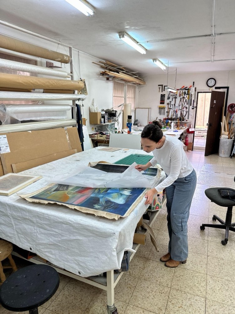 Stav Theodor at a print studio table, unwrapping a canvas