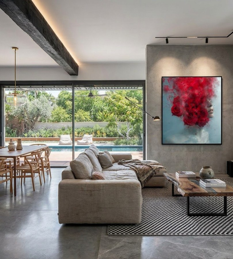 Open living space in a Hod Hasharon villa, a large figurative artwork of a woman's face dissolving into red roses on a concrete wall, garden and pool beyond the glass
