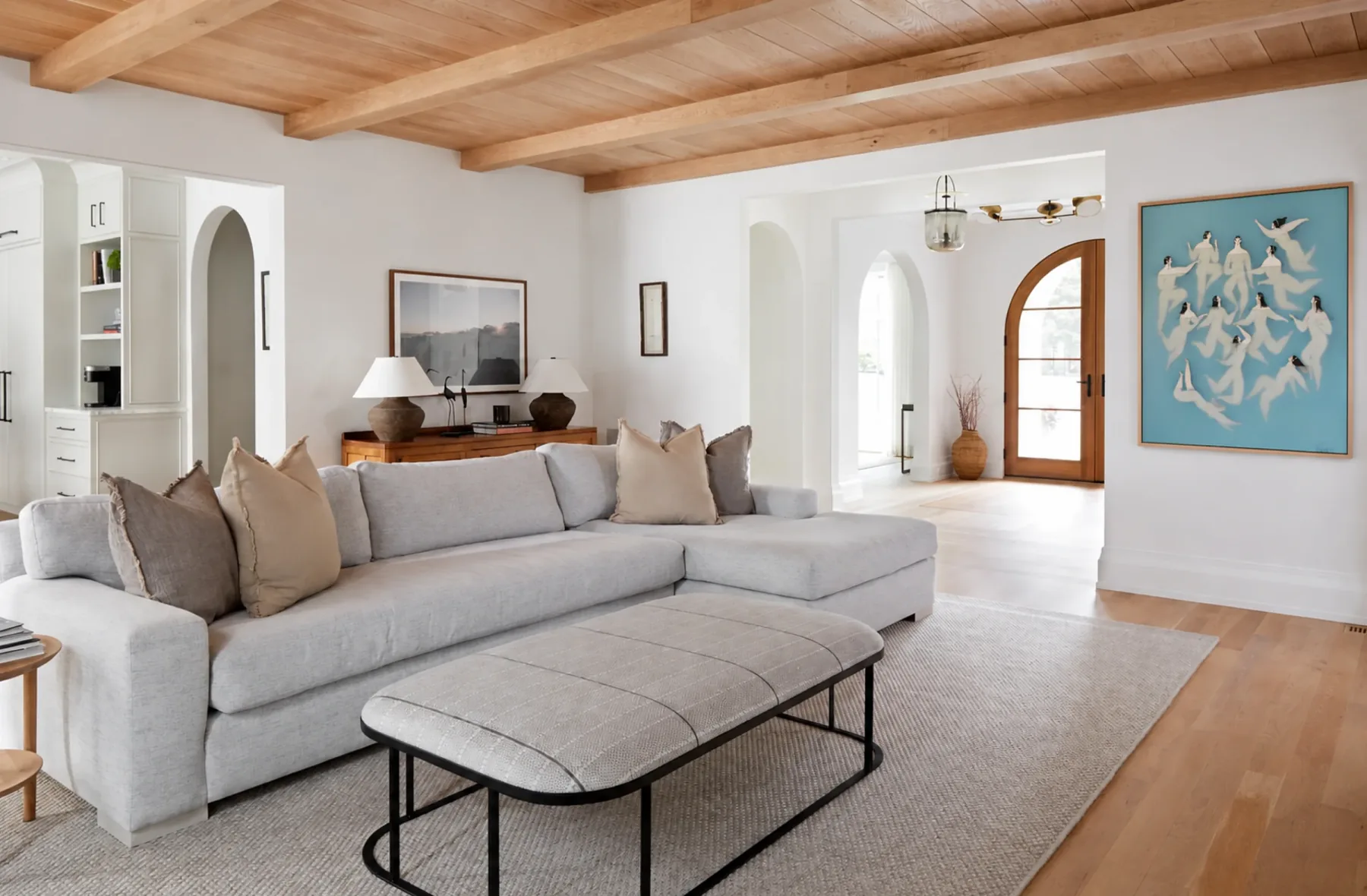 A white living room with a wood ceiling and a blue painting of swimmers on the right wall.