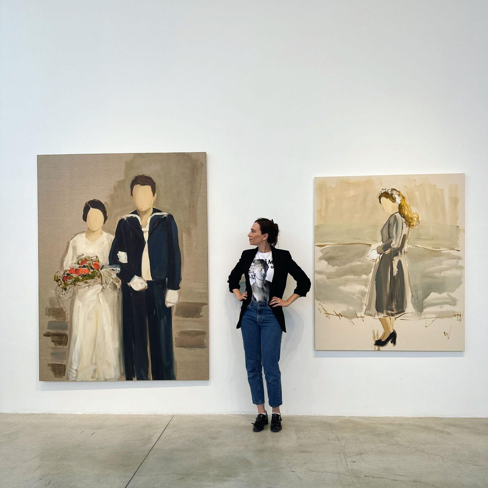 Stav Theodor standing between two large figurative paintings in a gallery