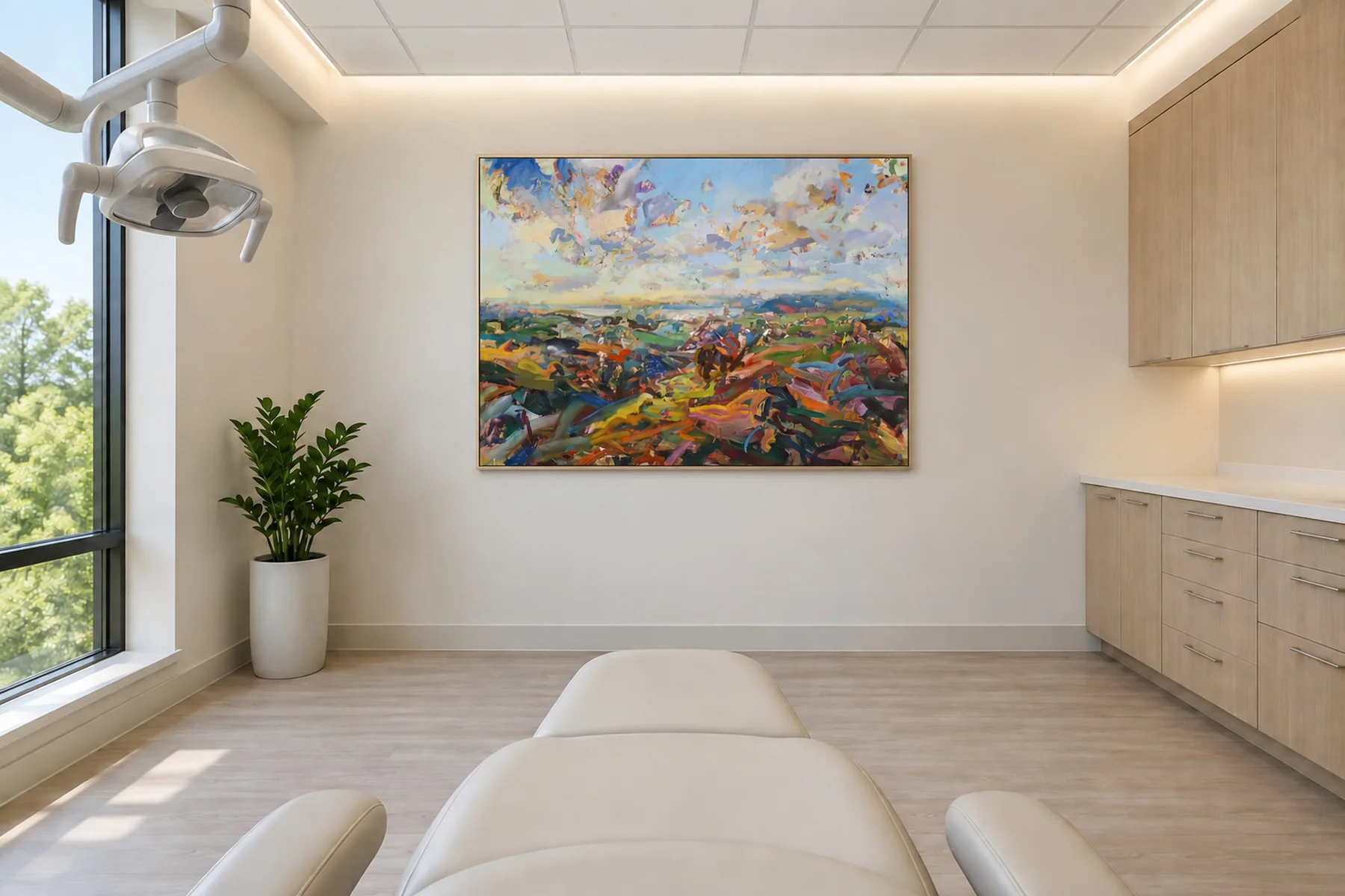 The view from a dental chair, sitting back: past the foot of the chair and the treatment light swung aside, a landscape painting of colorful hills and a bright sky hangs high on the facing wall, where the patient's eyes rest.